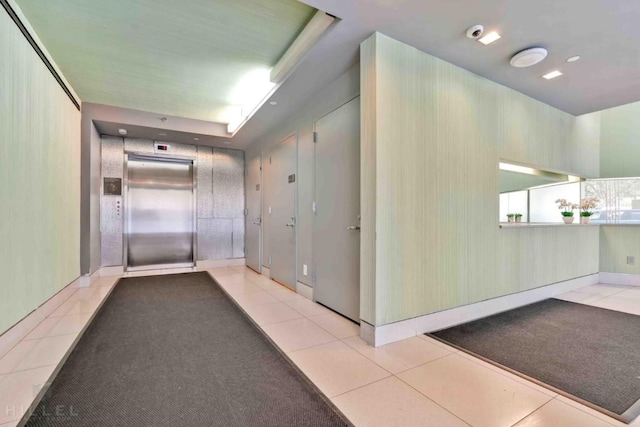 hall with elevator, a tray ceiling, and light tile patterned floors