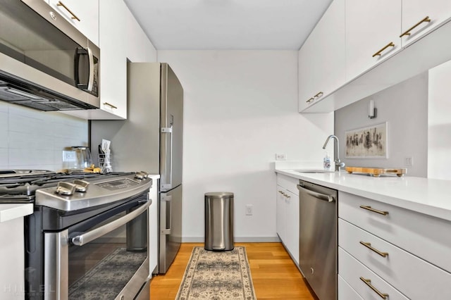 kitchen with appliances with stainless steel finishes, a sink, light countertops, tasteful backsplash, and modern cabinets