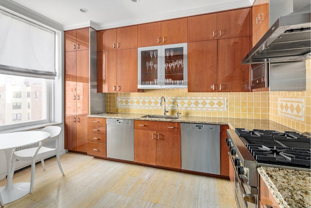 kitchen featuring backsplash, light stone counters, appliances with stainless steel finishes, wall chimney exhaust hood, and a sink