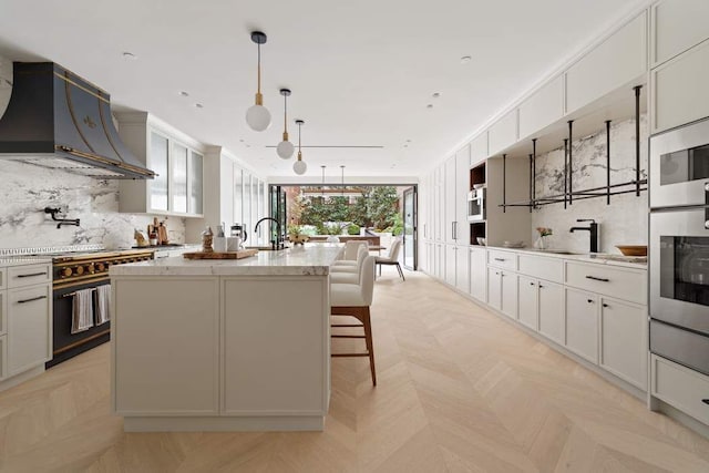 kitchen with high end range, white cabinetry, custom range hood, a center island with sink, and light parquet flooring