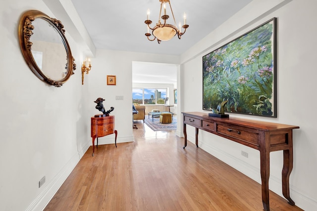 corridor with an inviting chandelier, light wood-style flooring, and baseboards