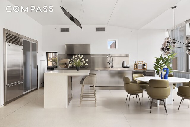 kitchen featuring lofted ceiling, a breakfast bar, sink, decorative light fixtures, and built in fridge