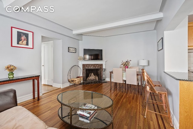 living area featuring beamed ceiling, a fireplace, wood finished floors, and baseboards