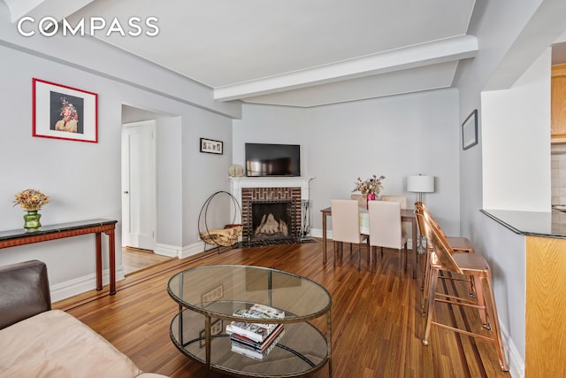 living room with baseboards, beam ceiling, wood finished floors, and a fireplace