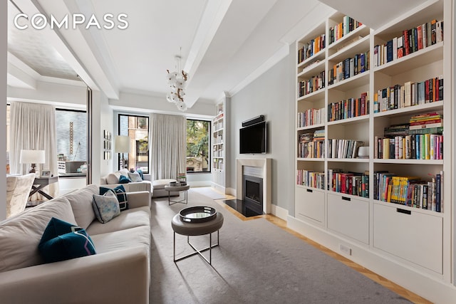 living room with a fireplace with flush hearth, wood finished floors, an inviting chandelier, crown molding, and baseboards