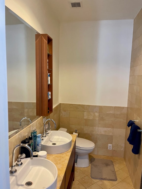 bathroom with tile patterned flooring, visible vents, tile walls, and a sink