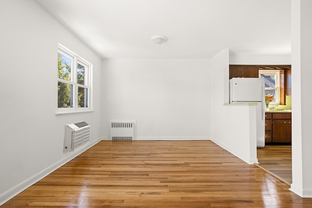 empty room with baseboards, radiator heating unit, heating unit, and light wood-style floors