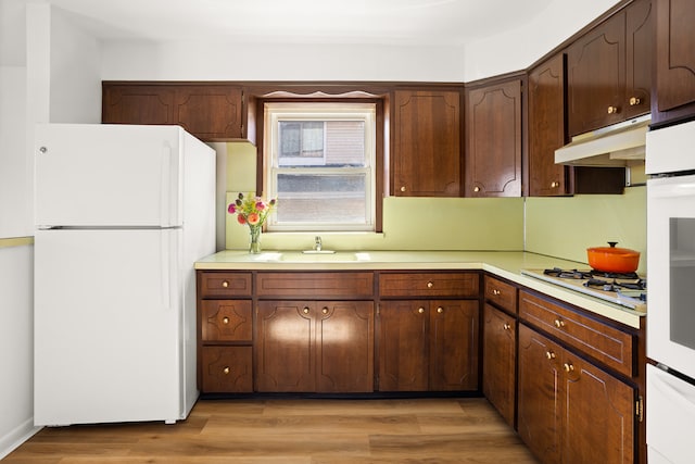 kitchen with white appliances, light wood finished floors, light countertops, under cabinet range hood, and a sink