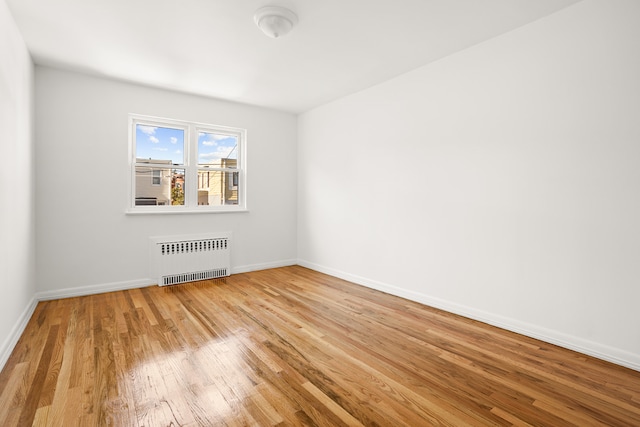 spare room featuring radiator heating unit, baseboards, and wood finished floors