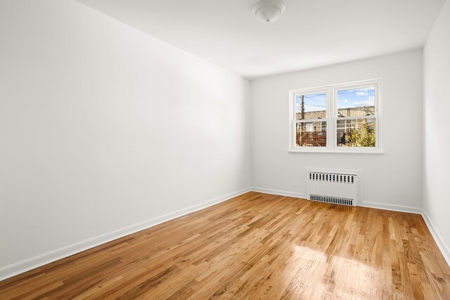 empty room featuring baseboards, light wood finished floors, and radiator