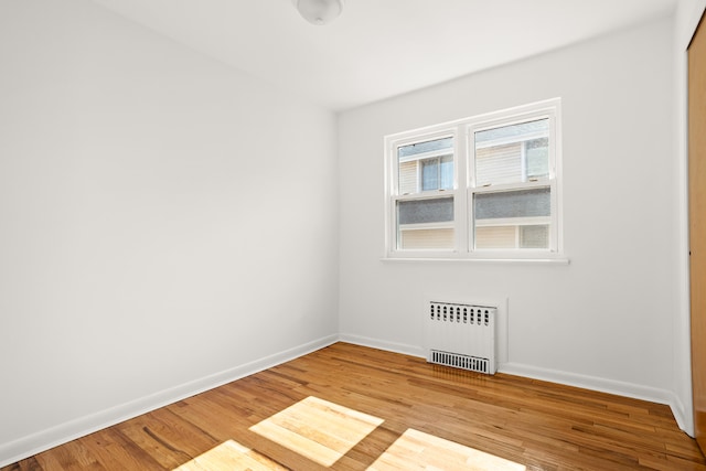 unfurnished room with baseboards, radiator heating unit, and wood finished floors