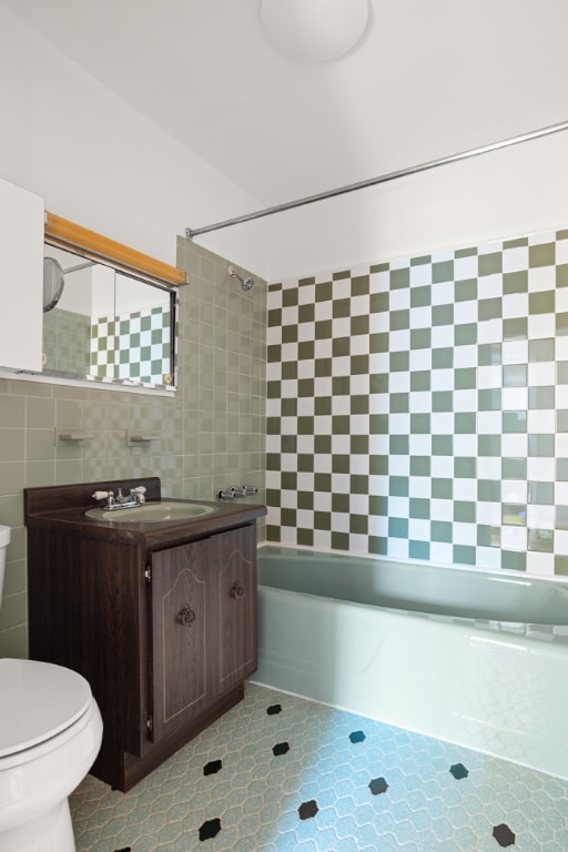 full bathroom with tile walls, toilet, vanity, and tiled shower / bath