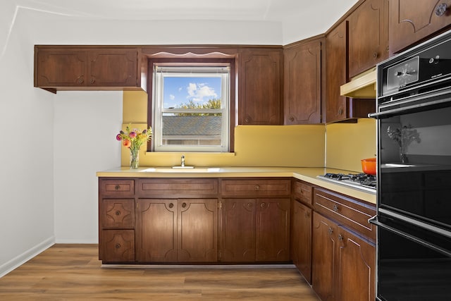 kitchen with stainless steel gas stovetop, light countertops, dobule oven black, under cabinet range hood, and a sink