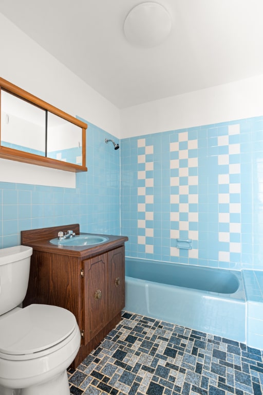 full bathroom with toilet, tile walls, vanity, and tiled shower / bath combo