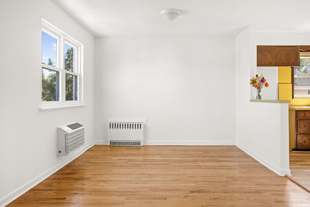 unfurnished room featuring light wood finished floors, a wealth of natural light, an AC wall unit, and radiator heating unit