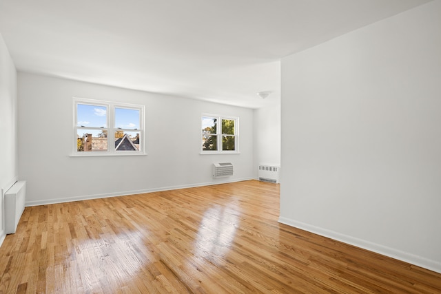 unfurnished room with baseboards, a wall mounted AC, light wood-style flooring, and radiator