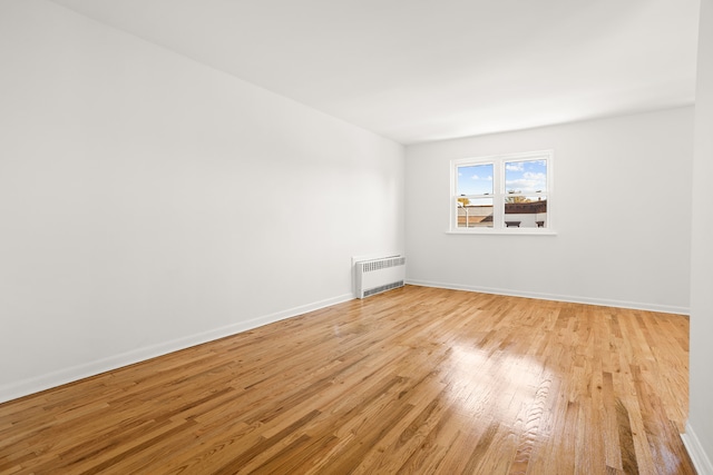 spare room with radiator, light wood-style flooring, and baseboards