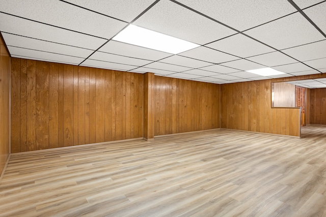 finished below grade area with wood finished floors, a drop ceiling, and wood walls
