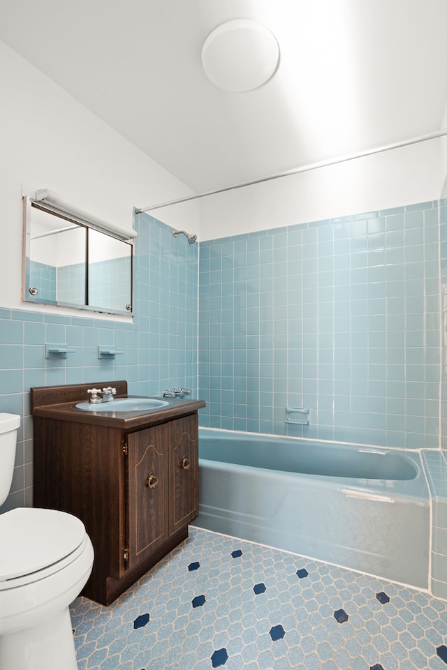 bathroom with washtub / shower combination, vanity, toilet, and tile walls