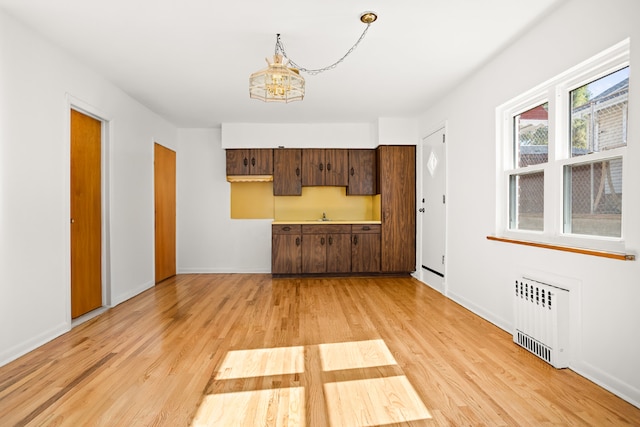 kitchen with light hardwood / wood-style floors, dark brown cabinetry, radiator heating unit, and a notable chandelier