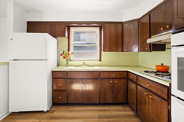 kitchen featuring light wood-type flooring, dark brown cabinetry, and white appliances