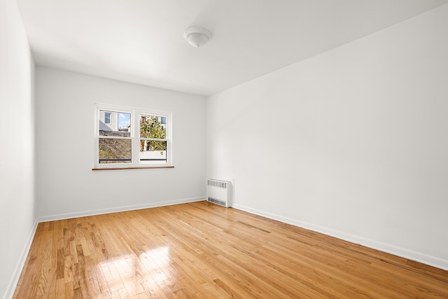 spare room with baseboards, light wood-style floors, and radiator heating unit