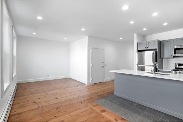 kitchen with stainless steel appliances, light countertops, baseboard heating, gray cabinetry, and a sink