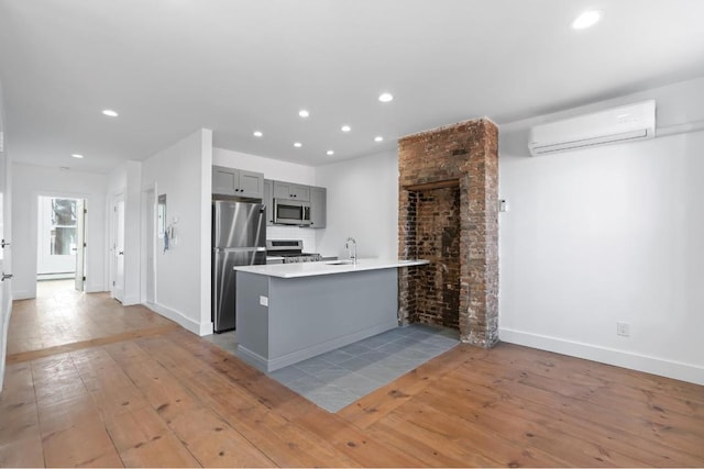 kitchen featuring stainless steel appliances, gray cabinets, light countertops, a wall mounted AC, and a peninsula