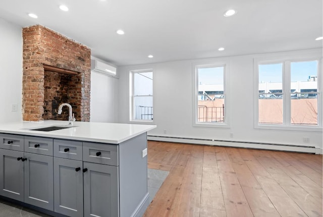 kitchen with a baseboard radiator, a wall mounted air conditioner, light countertops, gray cabinetry, and a sink