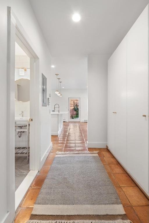 hall featuring light tile patterned floors, recessed lighting, a sink, electric panel, and baseboards