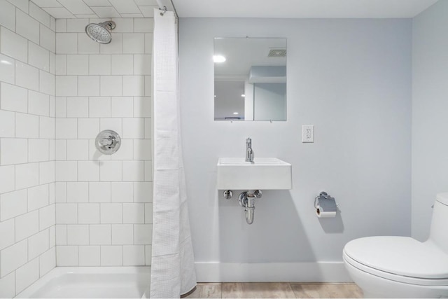 bathroom with toilet, baseboards, a tile shower, and wood finished floors