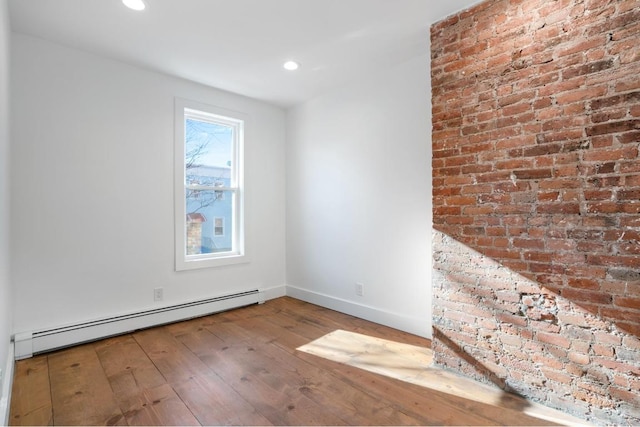 empty room with baseboards, brick wall, wood finished floors, baseboard heating, and recessed lighting