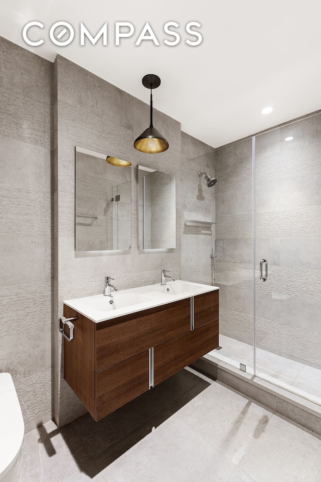 full bathroom with a sink, tile walls, a shower stall, and double vanity