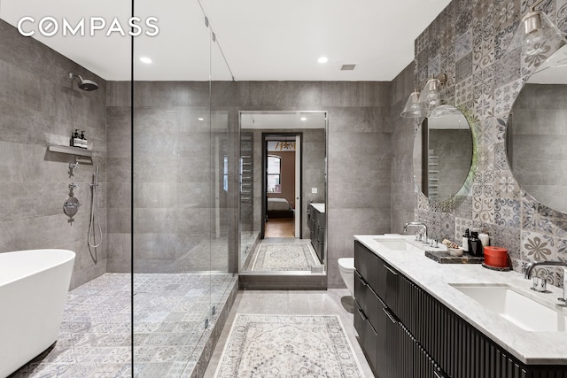 bathroom featuring a tile shower, double vanity, a sink, and tile walls