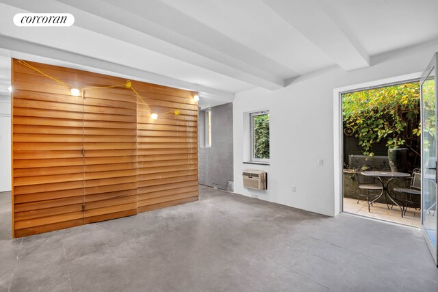 unfurnished living room featuring concrete flooring, a wall mounted AC, and beamed ceiling