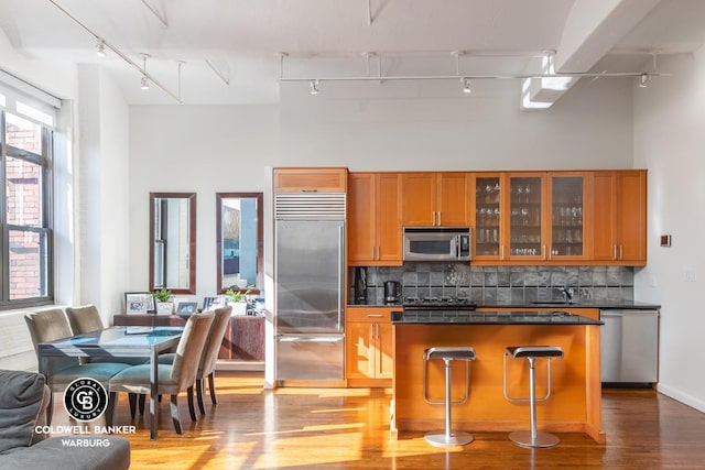 kitchen featuring appliances with stainless steel finishes, a kitchen island, decorative backsplash, rail lighting, and a breakfast bar area