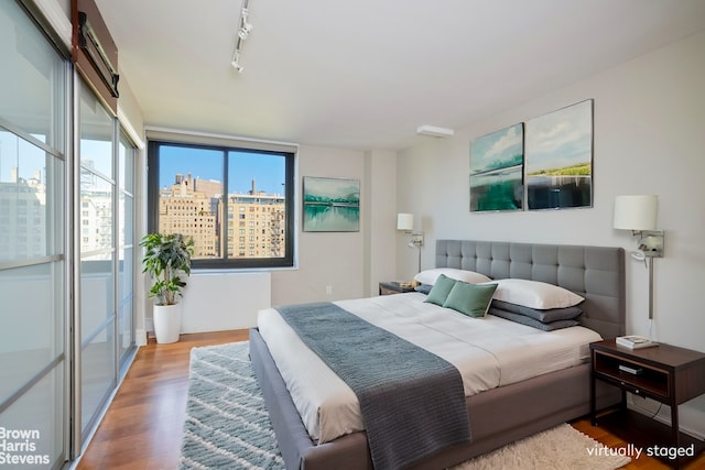 bedroom with track lighting, a view of city, and wood finished floors