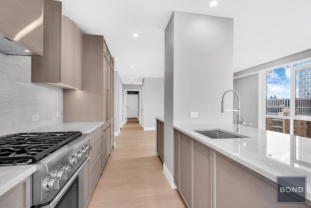 kitchen featuring light stone countertops, sink, stainless steel range with gas cooktop, and light hardwood / wood-style floors