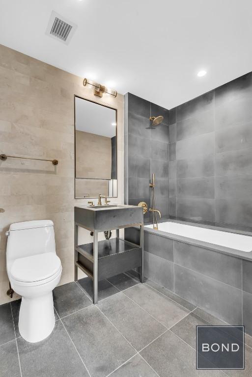 bathroom featuring tiled bath, toilet, and tile walls