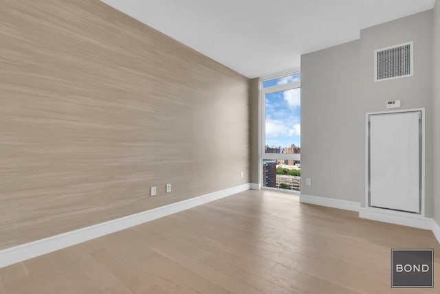 empty room with floor to ceiling windows and light hardwood / wood-style floors