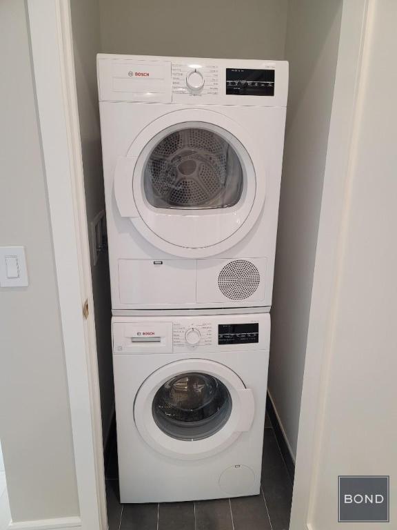 clothes washing area featuring stacked washer / dryer and dark tile patterned floors