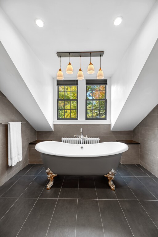 bathroom with tile walls, tile patterned flooring, a washtub, and radiator