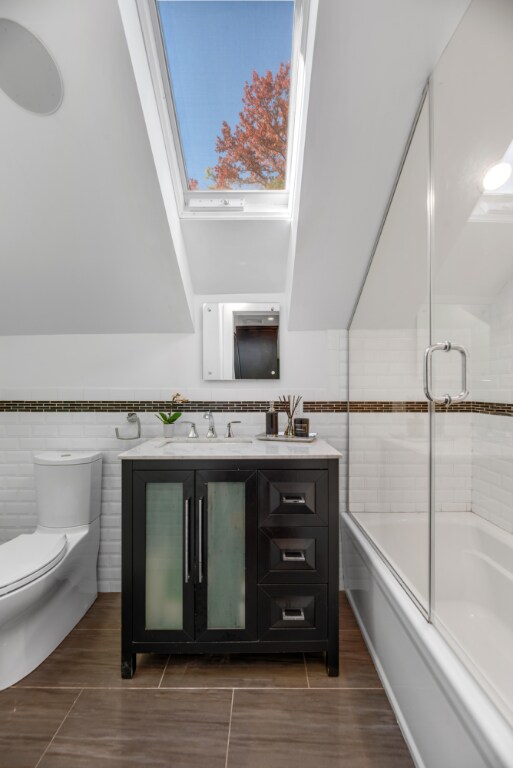 full bathroom with bath / shower combo with glass door, vanity, tile walls, and toilet