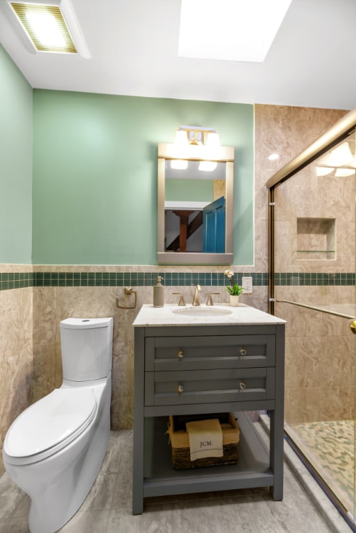 bathroom featuring tile walls, vanity, a tile shower, and a skylight