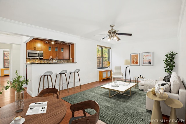 living area with a ceiling fan, crown molding, baseboards, and wood finished floors