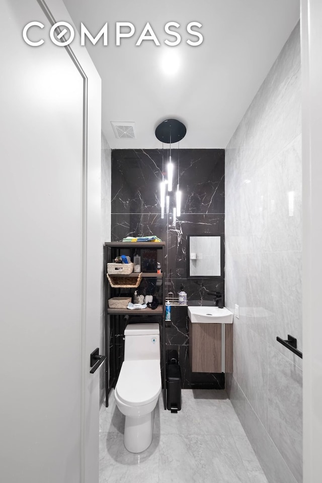 bathroom with toilet, marble finish floor, visible vents, and tile walls