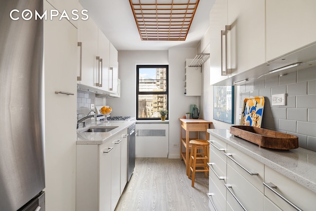 39 Gramercy Park N Unit 9A, New York City, NY 10010 - kitchen featuring appliances with stainless steel finishes, decorative backsplash, light wood-type flooring, a sink, and white cabinetry