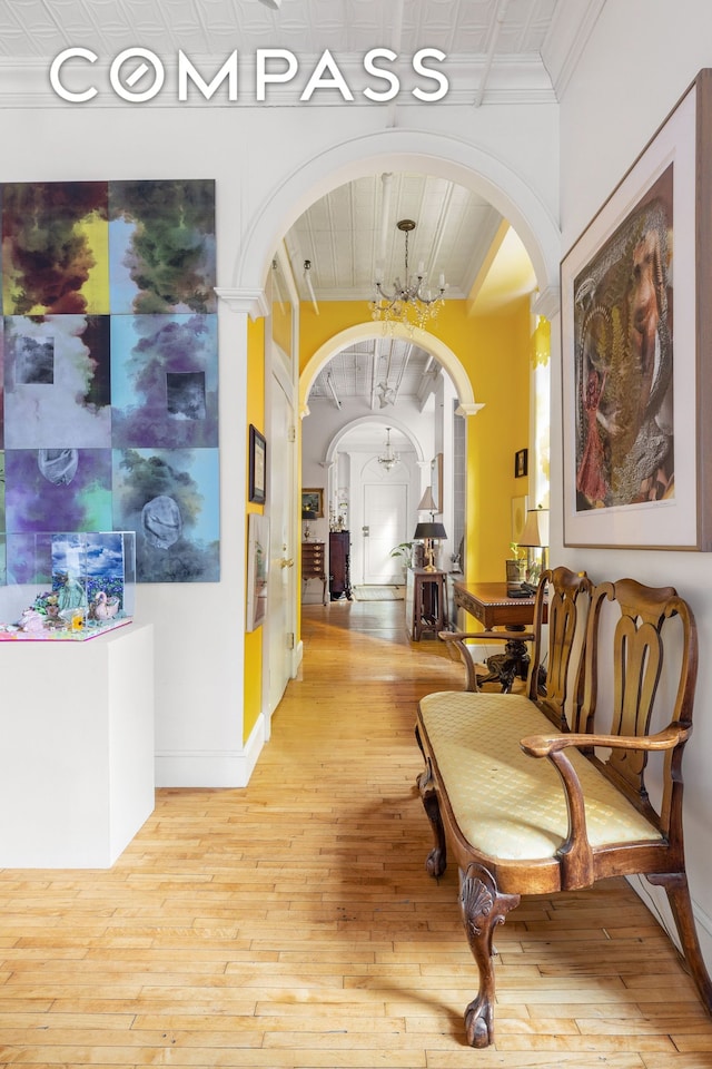 hallway featuring arched walkways, crown molding, a chandelier, light wood-style flooring, and baseboards