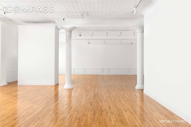 basement featuring rail lighting, a decorative wall, and light wood-style flooring