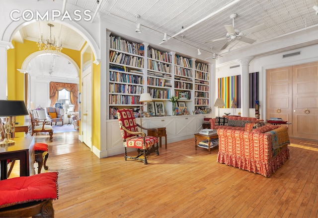living area featuring decorative columns, wood-type flooring, track lighting, and arched walkways